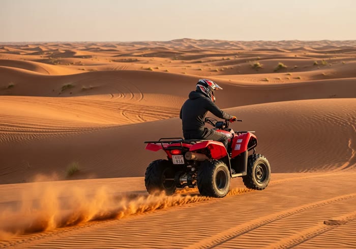 Single-seater quad bike kicking up sand at sunset