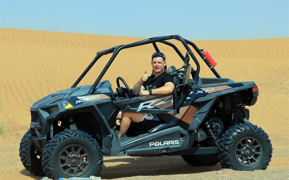 Dune buggy on red desert dunes at sunset